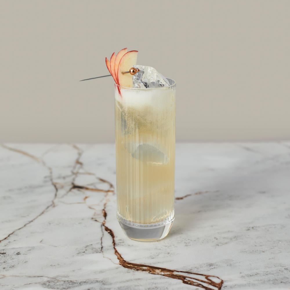 Seedlip non-alcoholic cocktail served in a tall glass with ice and garnished with apple slices on a marble surface