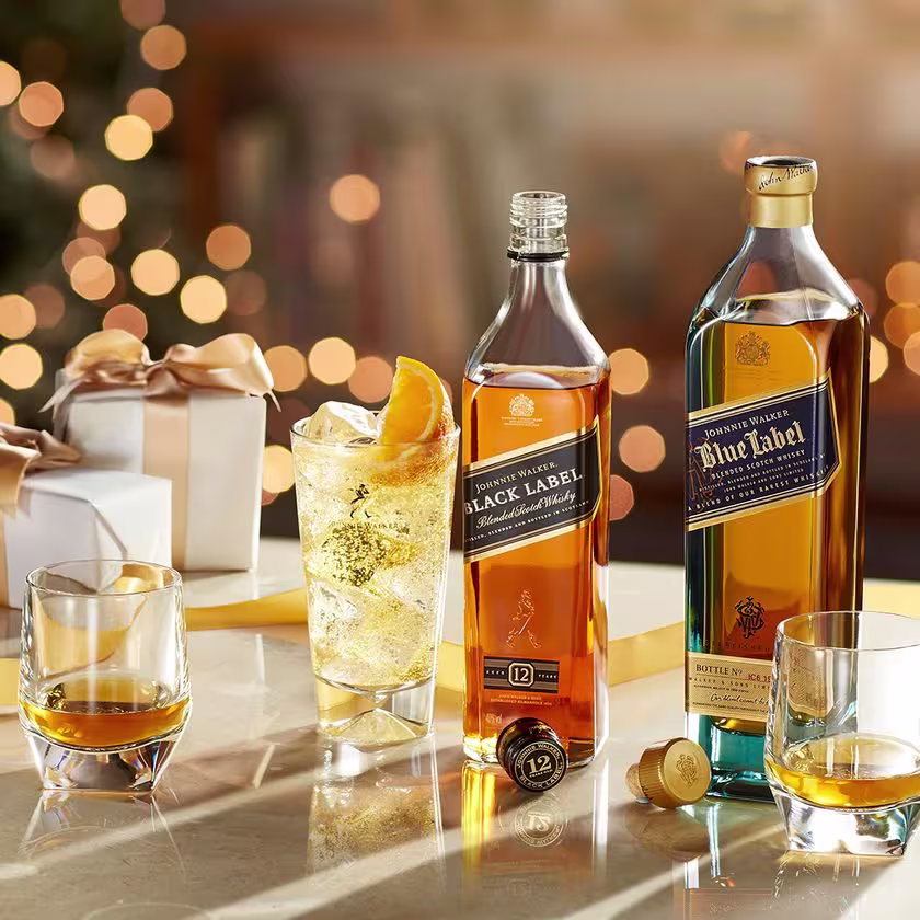 La foto muestra una botella de whisky Johnnie Walker Black Label y otra botella de whisky Johnnie Walker Blue Label, junto a tres vasos con diferentes cócteles.
