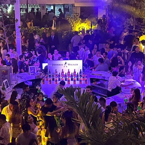 Imagen de una fiesta en la cual en el centro hay una barra circular de la marca Johnnie Walker. Además, algunas plantas alrededor
