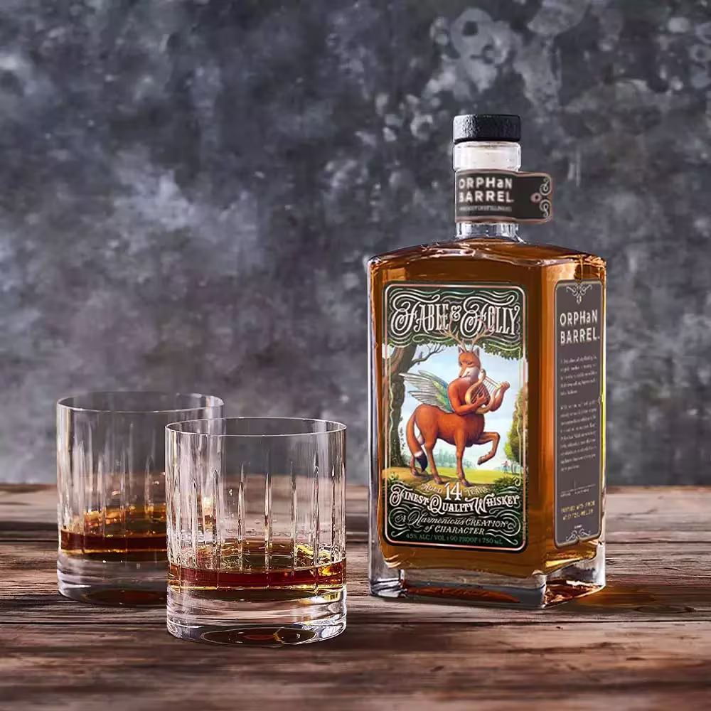 A bottle of Orphan Barrel Fable & Folly whiskey sits on a wooden surface next to two glasses containing whiskey, with a textured gray background.