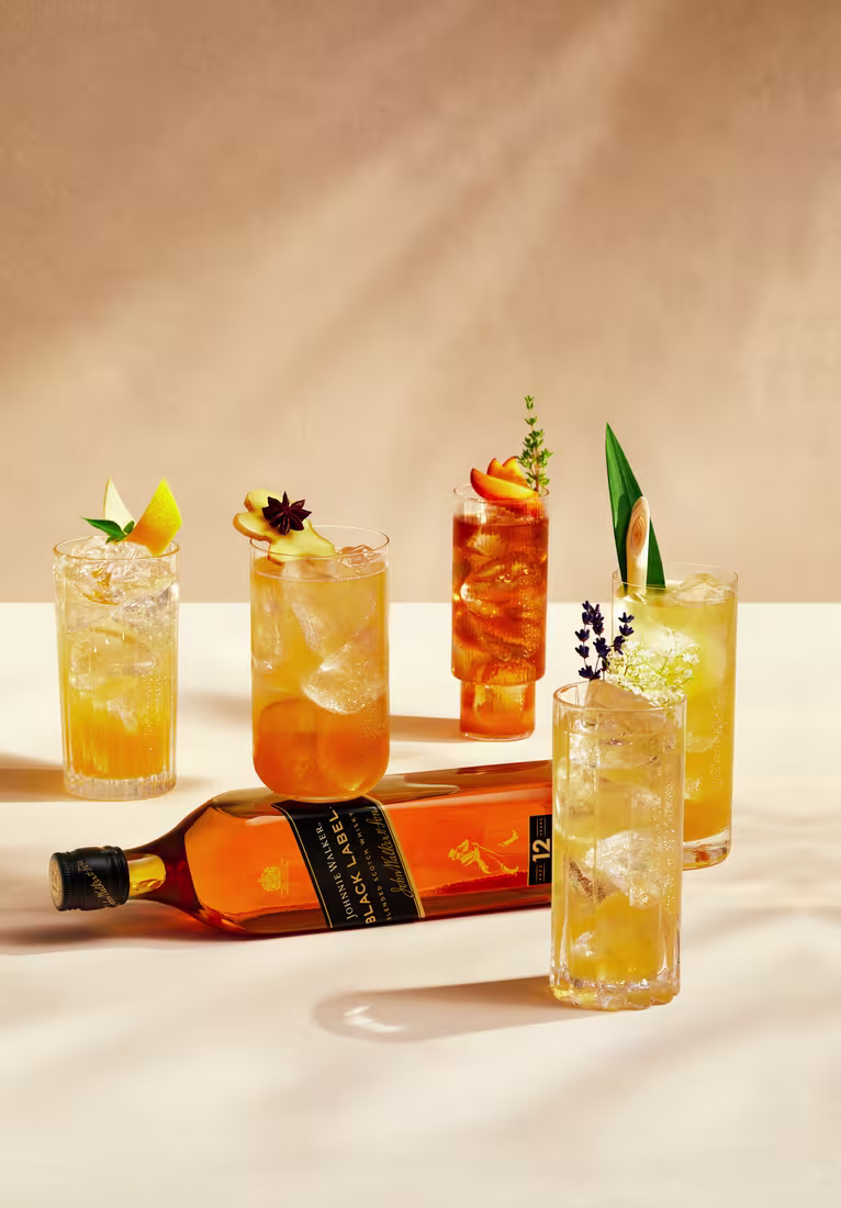 La imagen muestra cinco cócteles diferentes preparados con whisky Johnnie Walker Black Label, acompañados de la botella de dicho whisky colocada de forma horizontal.