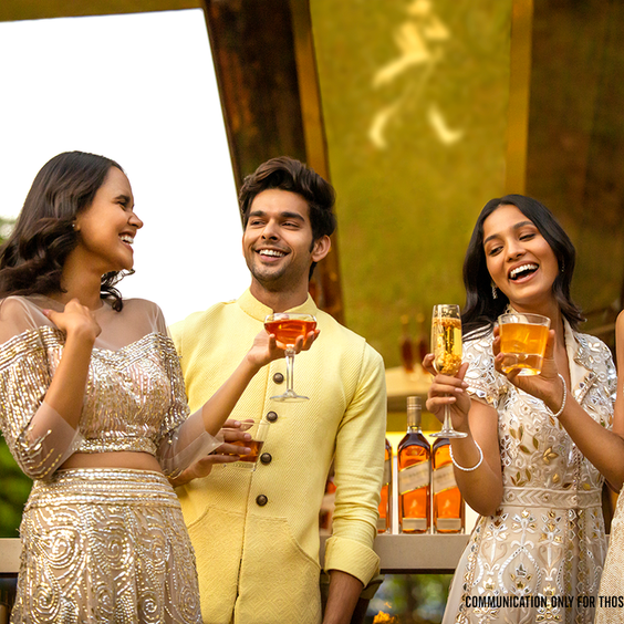 Cuatro personas sostienen diferentes cócteles mientras, en el fondo difuminado, se observan botellas de whisky Johnnie Walker Gold Label Reserve.
