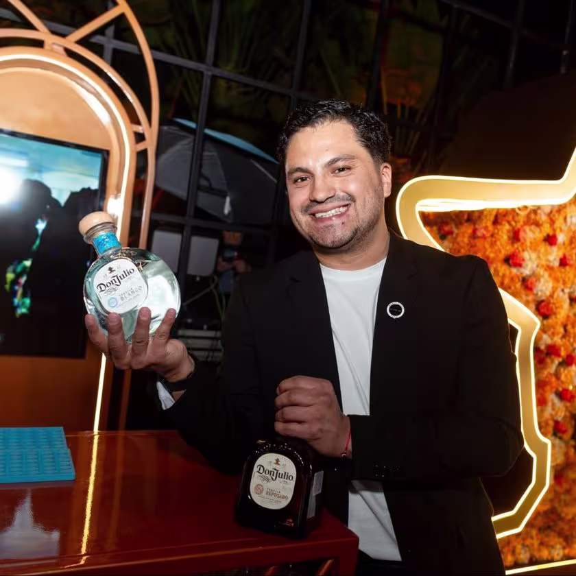La imagen muestra una persona con una botella de tequila Don Julio Blanco en una mano y con una botella de tequila Don Julio Reposado en la otra.