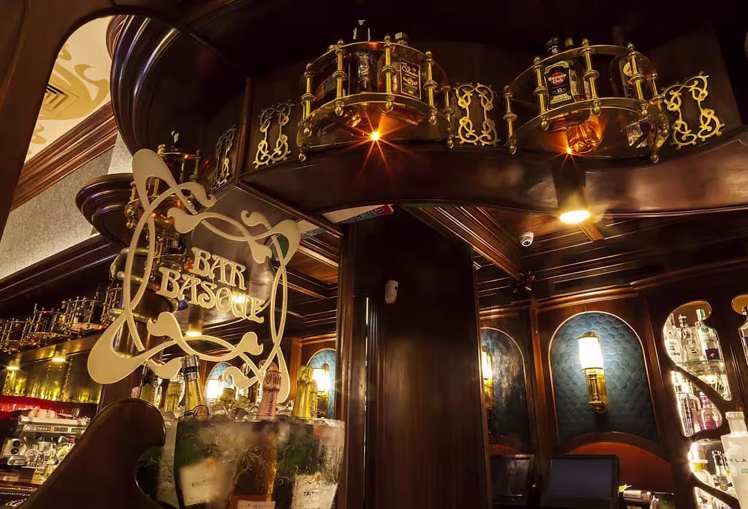 Bar Basque destaca con su elegante barra de madera oscura, vitrinas doradas y botellas premium. Un rincón sofisticado y acogedor.