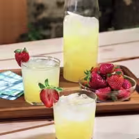 La imagen muestra una botella y dos vasos rellenos con un cóctel preparado con vodka y fresas alrededor.