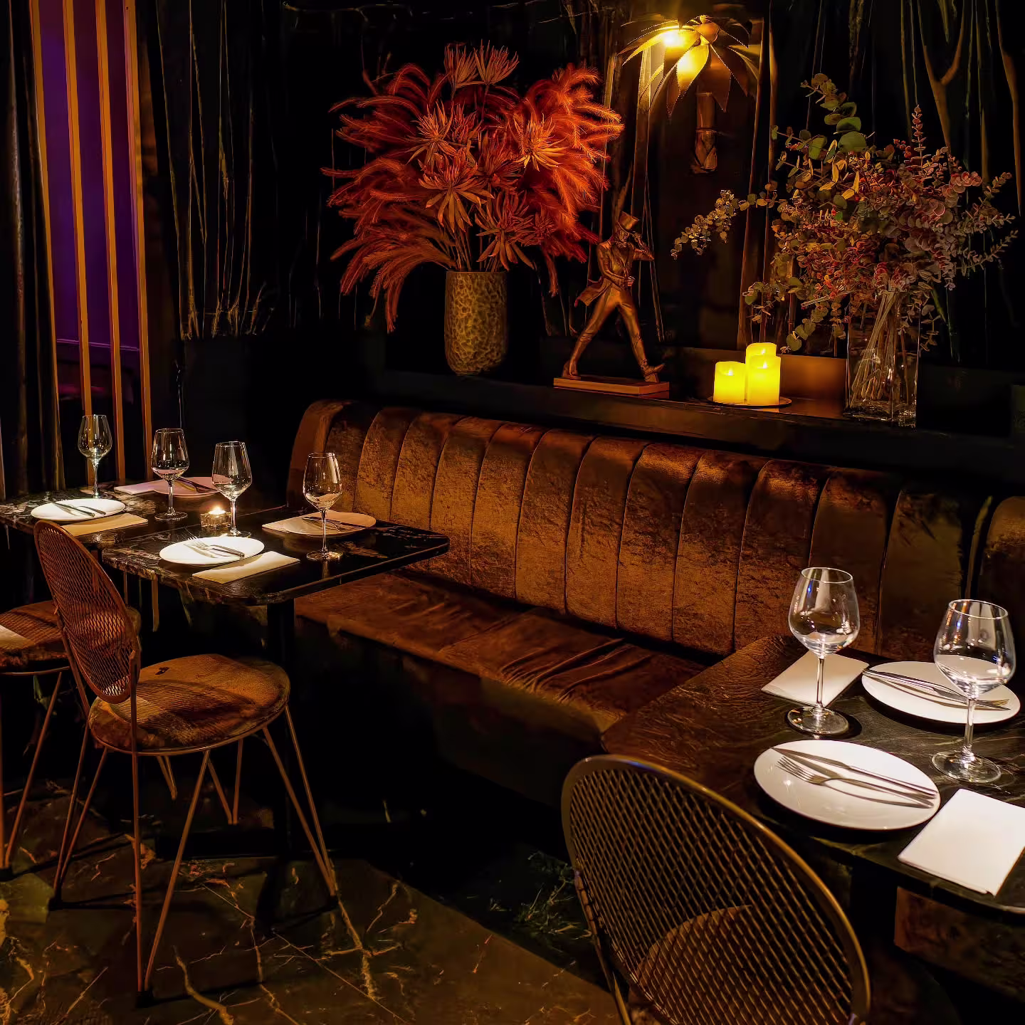 Interior de La Perla con sofá aterciopelado, mesas negras elegantes, sillas de diseño, flores decorativas y velas creando ambiente íntimo.