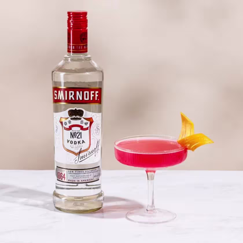 La imagen muestra una botella de vodka Smirnoff n°21 junto a una copa rellena con el cóctel Cosmopolitan.