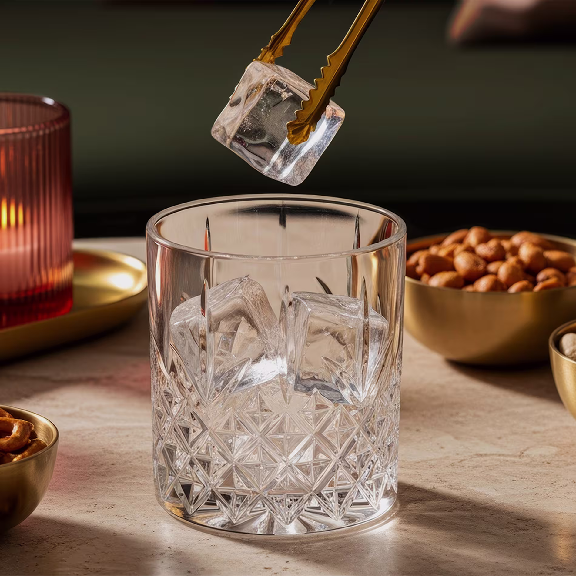 Tongs dropping ice cubes into a rocks glass