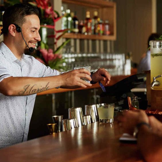 La imagen muestra un bartender sirviendo tragos detrás de una barra.