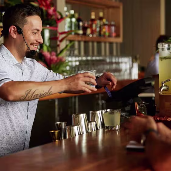 La imagen muestra un bartender sirviendo tragos detrás de una barra.