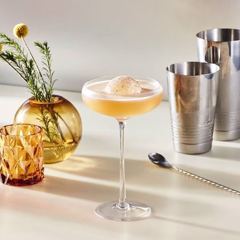 La imagen muestra una copa rellena con el cóctel Whisky Sour y otros elementos de coctelería alrededor.