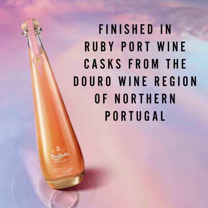 The image displays a sleek bottle of Don Julio Rosado tequila set against a soft gradient background of pink and blue hues. The text on the image reads: "Finished in Ruby Port Wine Casks from the Douro Wine Region of Northern Portugal," highlighting the unique aging process of this tequila.
