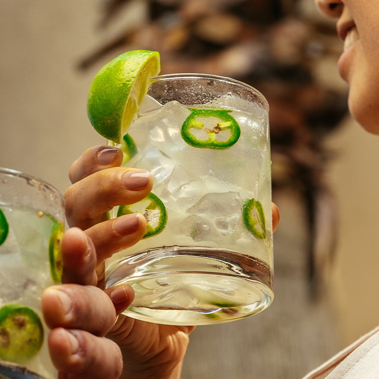 Două persoane țin cocktailuri margarita picante în pahare cu gheață.