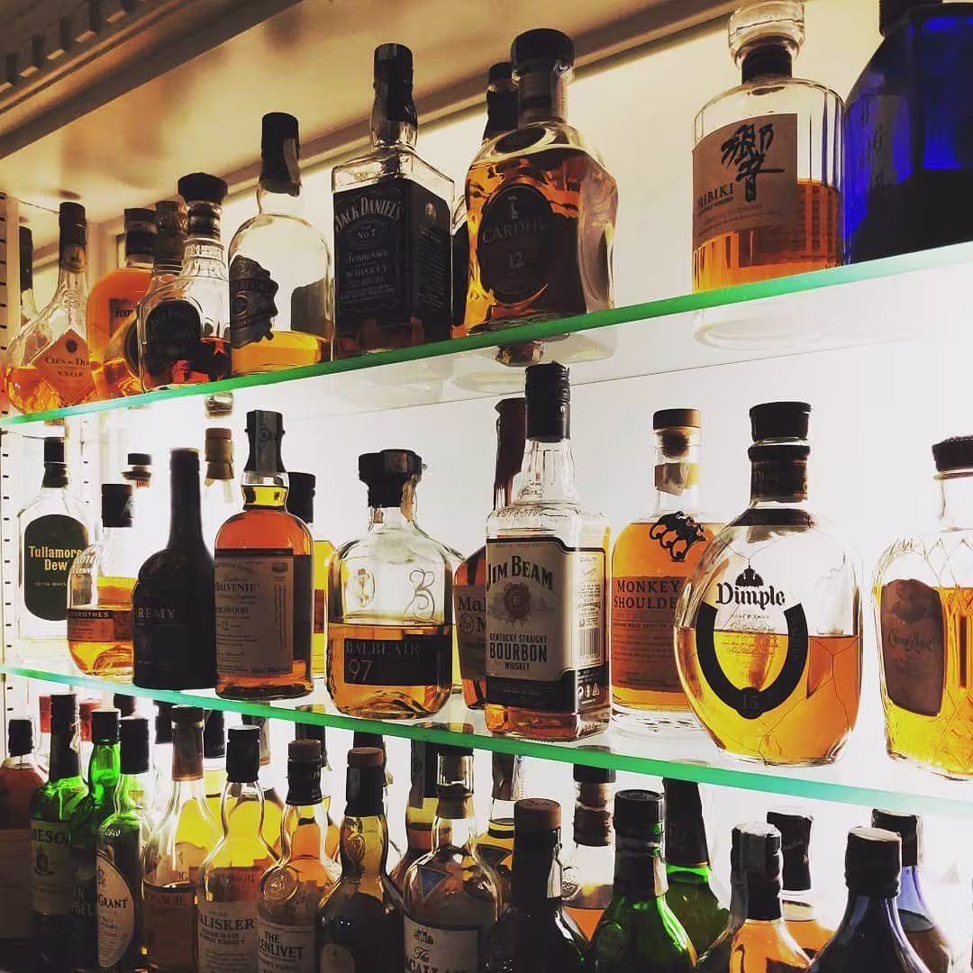 La imagen muestra una estantería iluminada del Bar Jaime con una variada colección de botellas de whisky y licores premium, destacando marcas icónicas.