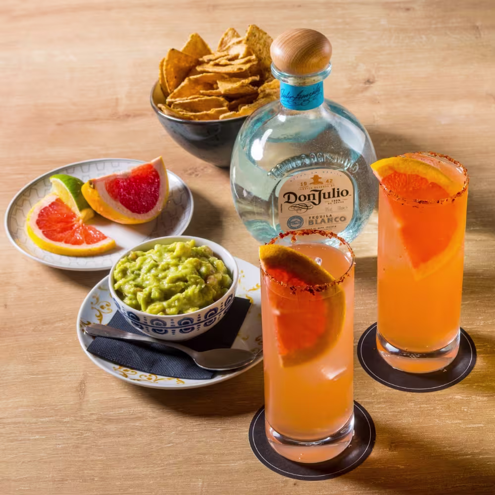 Mesa con aperitivos mexicanos y vasos con bebida naranja.