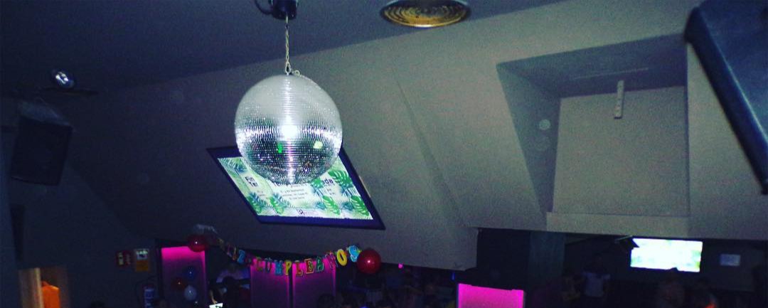 Fiesta en Parkim Bar con bola de espejos, luces de ambiente y asistentes disfrutando de una noche animada.
