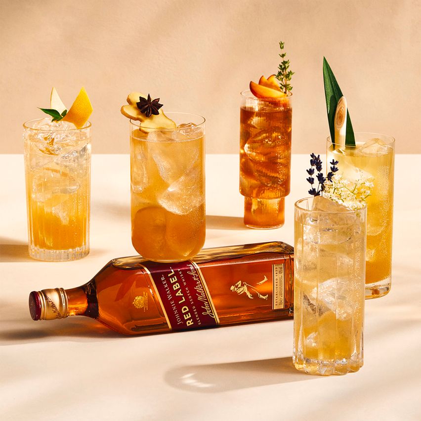En la imagen se puede apreciar cinco vasos estilo highball de diferentes formas con una botella whisky Johnnie Walker Red Label apoyada de costado.