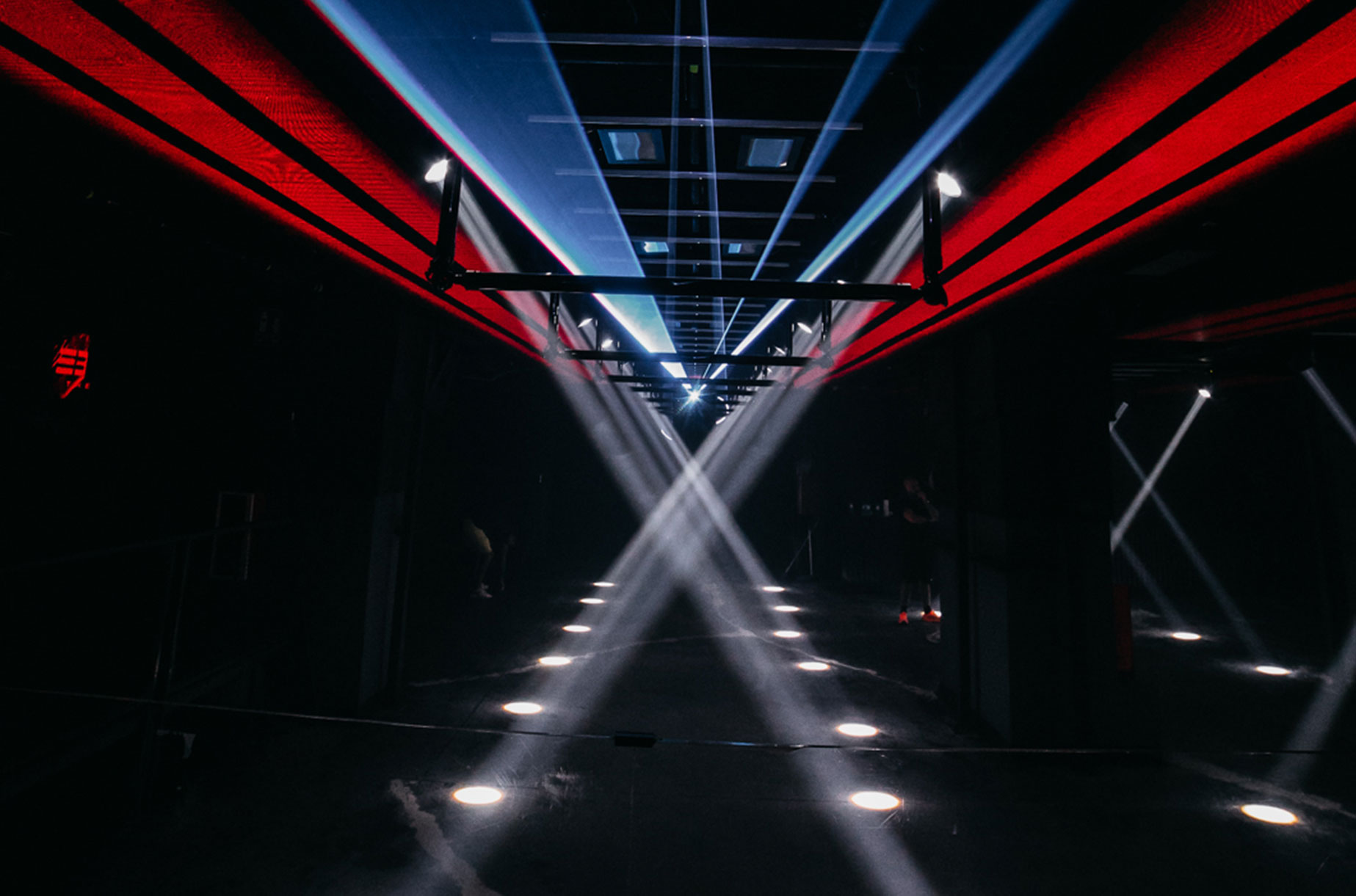 The Basement muestra un pasillo oscuro con luces blancas cruzadas y paneles rojos en el techo, creando una atmósfera futurista y minimalista.