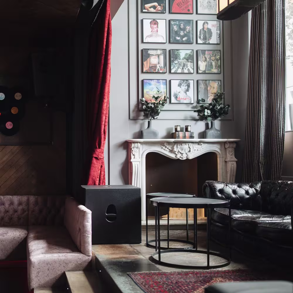 Interior de Bardot, con sofás acolchados, detalles vintage como discos de vinilo y una chimenea ornamental, creando un ambiente íntimo y sofisticado.
