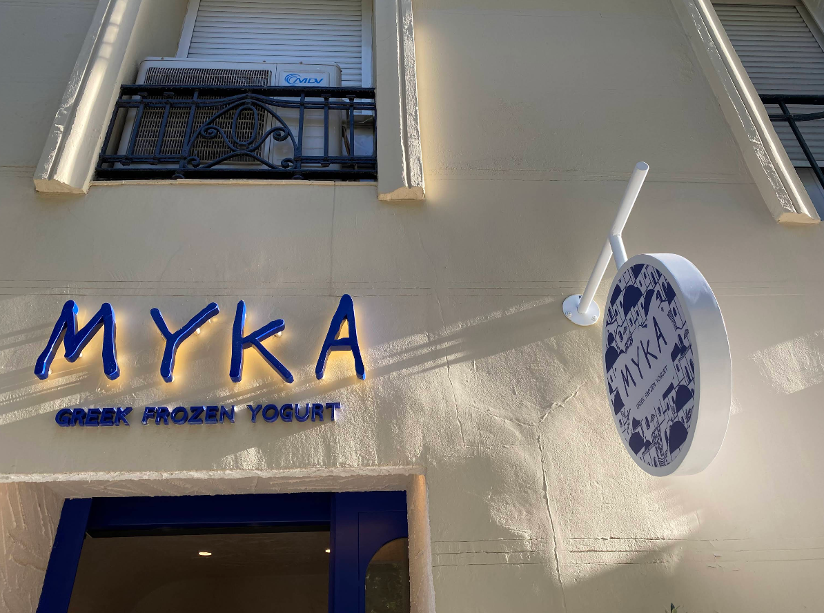 Fachada de Myka Ortega y Gasset con letras azules retroiluminadas y rótulo circular decorado con motivos griegos.