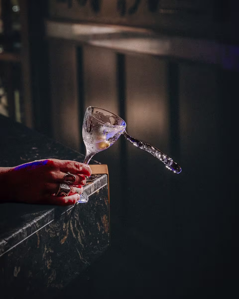 Escena en Bar Sauvage con mano sosteniendo copa de cóctel adornada con hielo en espiral, sobre una barra de mármol oscuro.