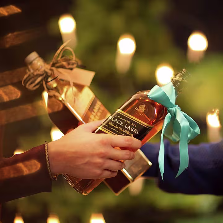 La imagen muestra dos botellas de whisky Johnnie Walker Black Label cada una con un moño de regalo.