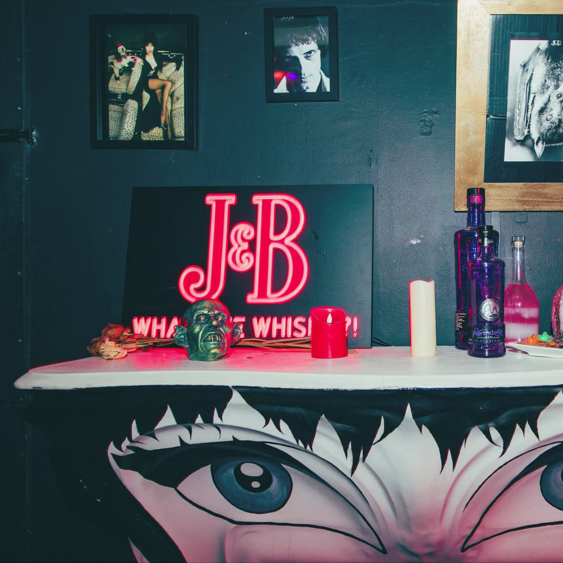 " Mesa decorada con temática oscura, luces de neón, botellas y detalles siniestros, creando una atmósfera intrigante y teatral."
