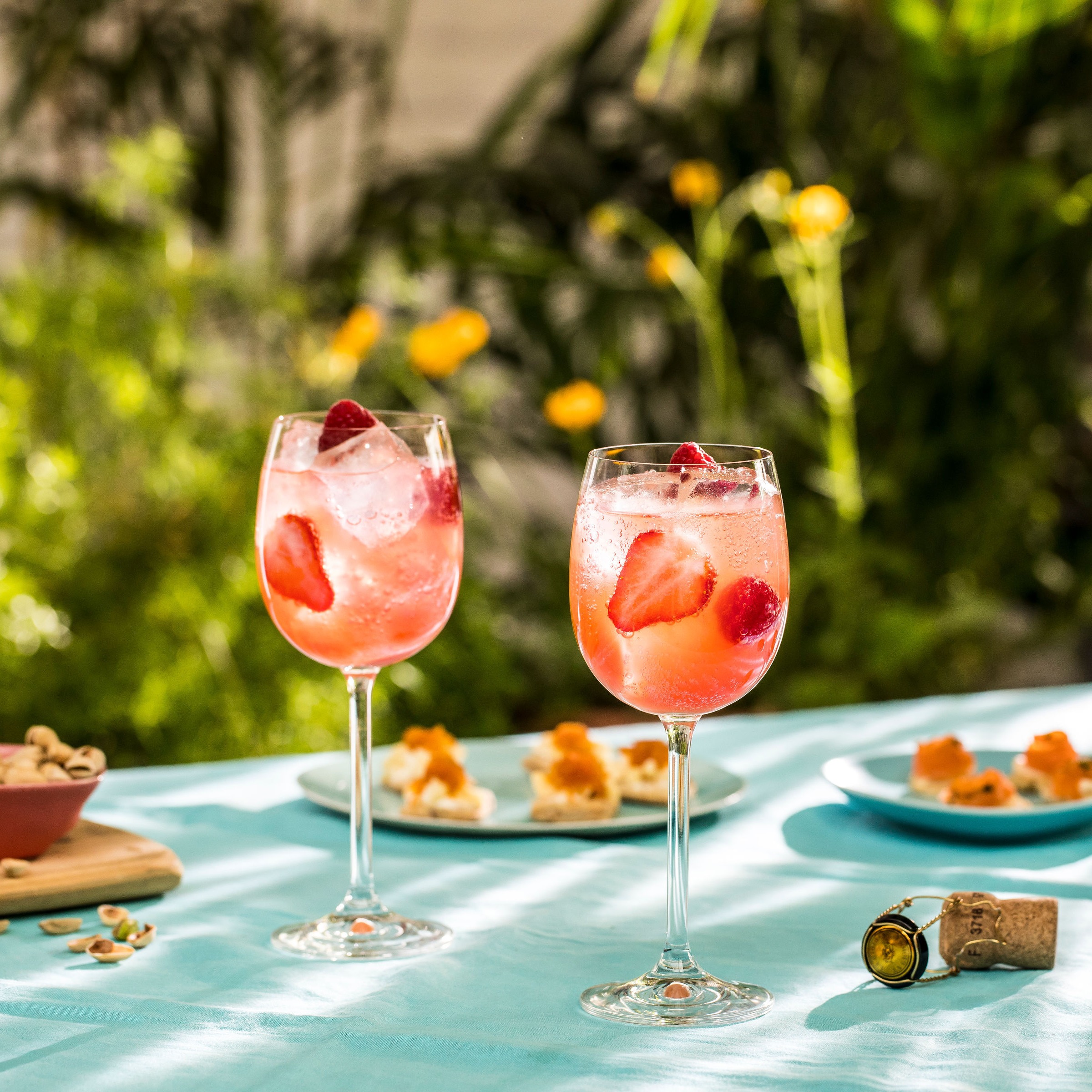 Two pink gin and tonic drinks on a table in a green leafy garden. 