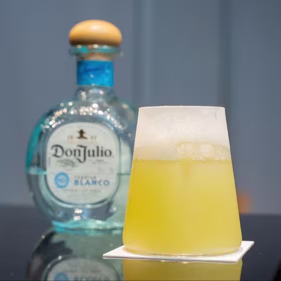 La imagen muestra una botella de tequila Don Julio Blanco junto a un vaso con un cóctel llamado "Margarita Costera" creado por el finalista de World Class 2024 Perú, Rolando Arias de Troppo.