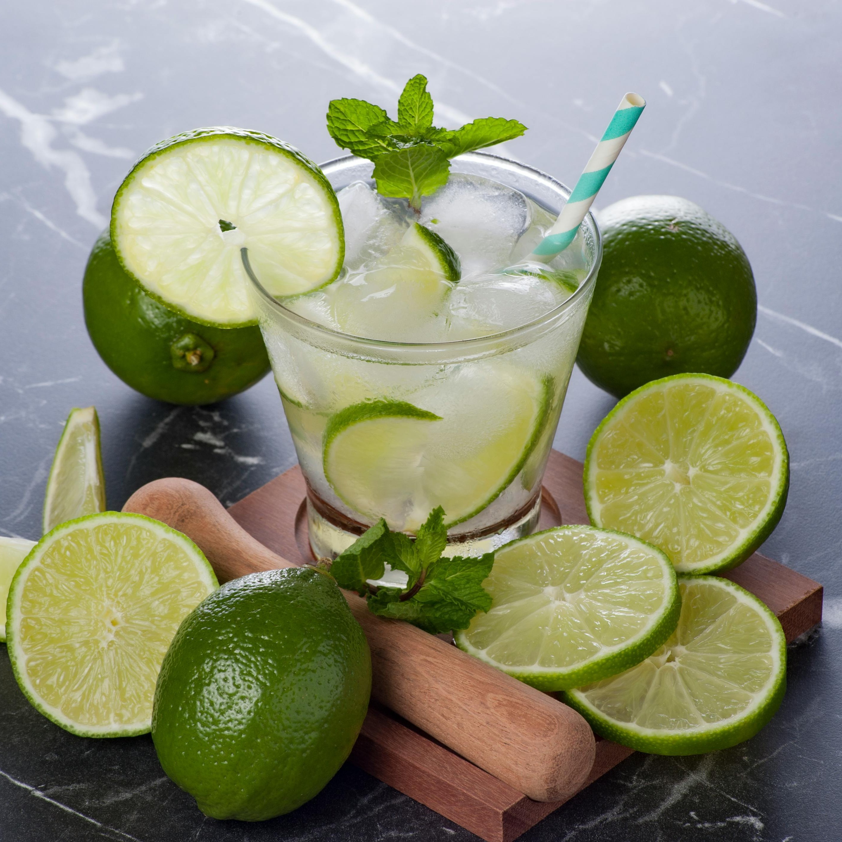 A nojito cocktail sits on a wooden board, surrounded by sliced limes.