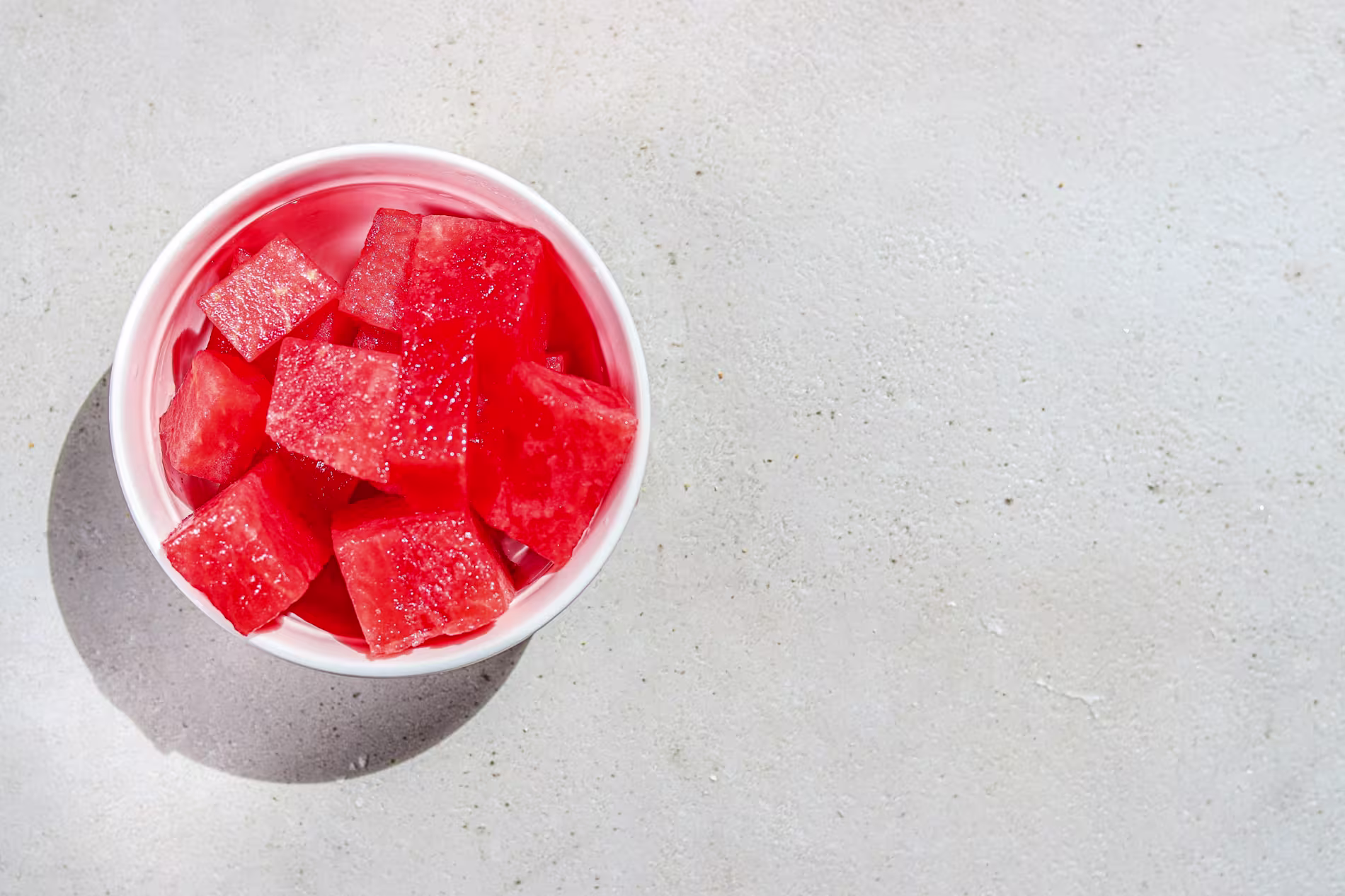 A white bowl filled with cubed watermelon sits on a light, textured surface.
