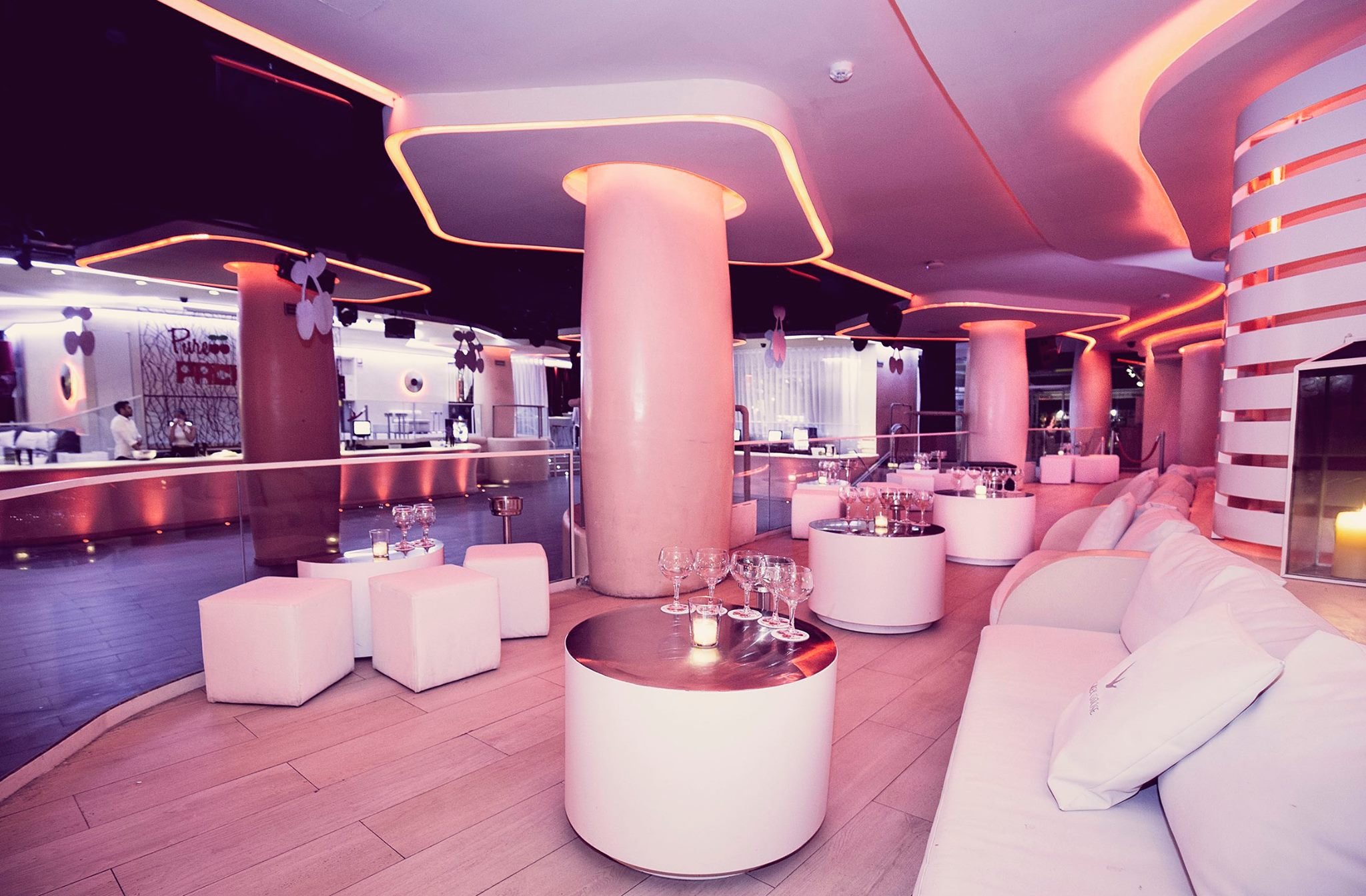 Interior de Pacha Barcelona, con diseño moderno en tonos blancos y rosados, sofás acolchados, mesas redondas y luces ambientales cálidas.