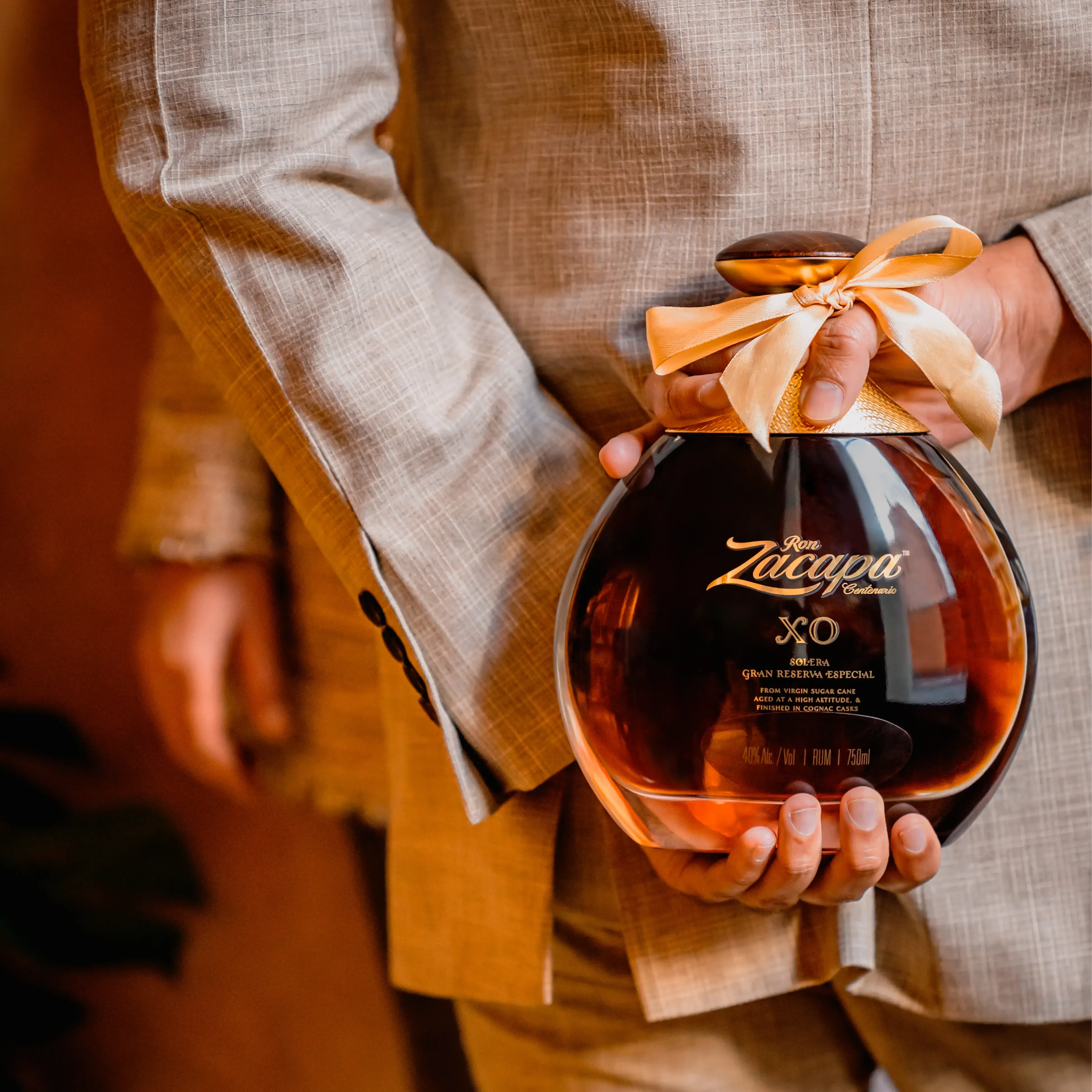 Cada regalo esconde una historia, botella de zacapa con lazo dorado escondida en la espalda de alguien que va a regalarla. 