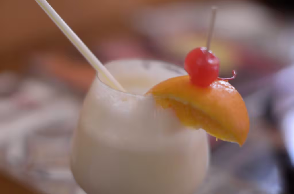 A creamy drink in a stemmed glass, garnished with an orange slice and a maraschino cherry, with a straw inserted.
