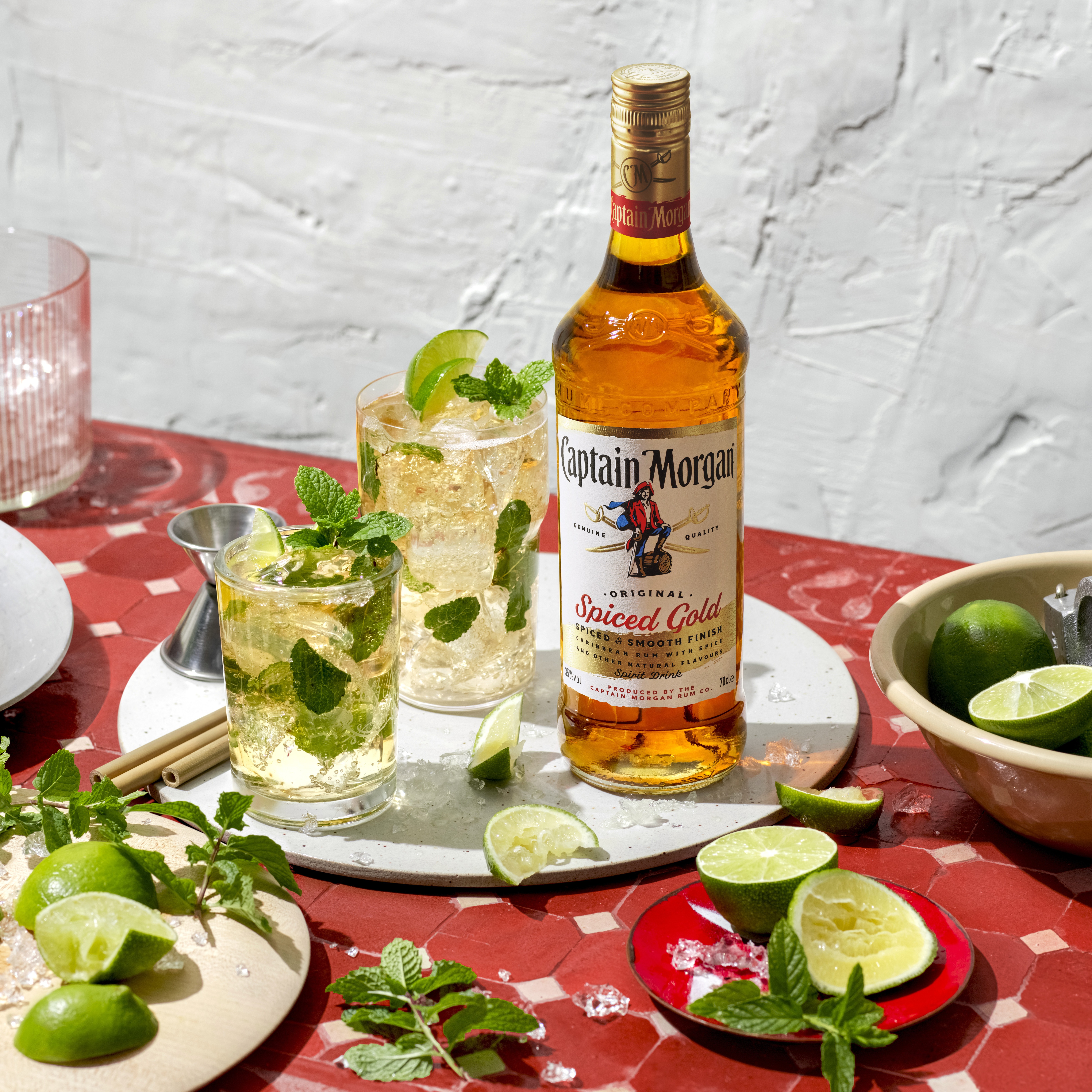 A bottle of Captain Morgan Original Spice Rum next to two mojitos and assorted plates of food.