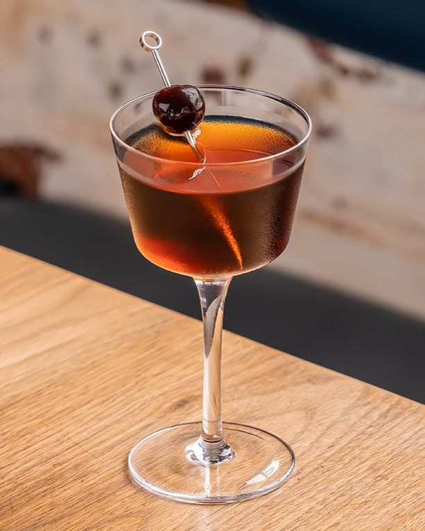 Un cocktail Manhattan într-un pahar coupette cu o garnitură de cireșe