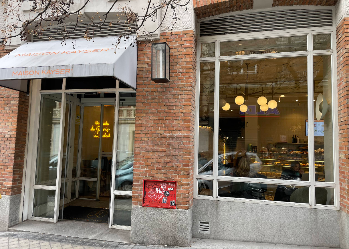 Fachada de Maison Kayser en Gaztambide con grandes ventanales, toldo blanco y vistas al interior, donde se aprecia el ambiente cálido y luminoso.