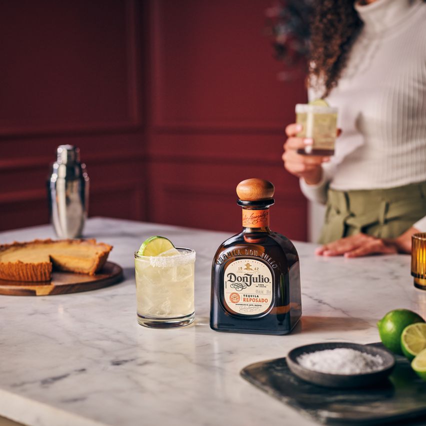 La imagen muestra una botella de tequila Don Julio Reposado junto a un vaso con el cóctel Margaria Don Reposado y otros elementos de coctelería.
