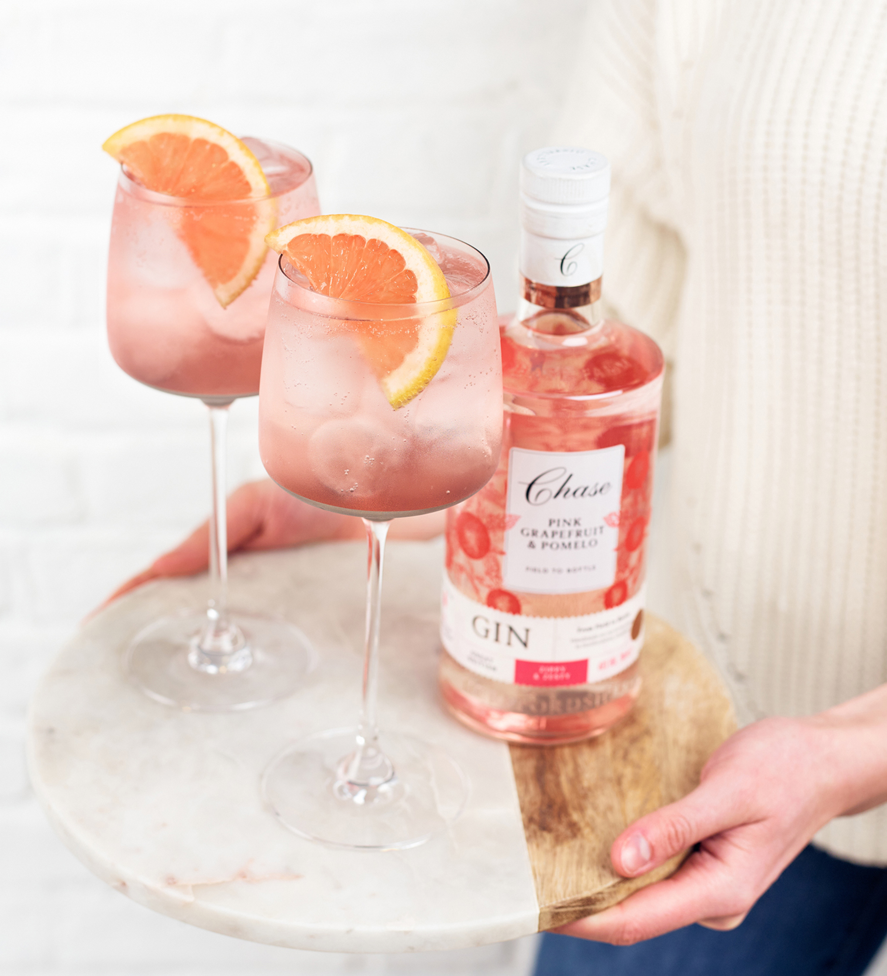 Chase Pink Grapefruit & Pomelo Gin bottle with two spritz cocktails garnished with grapefruit slices, served on a marble tray.
