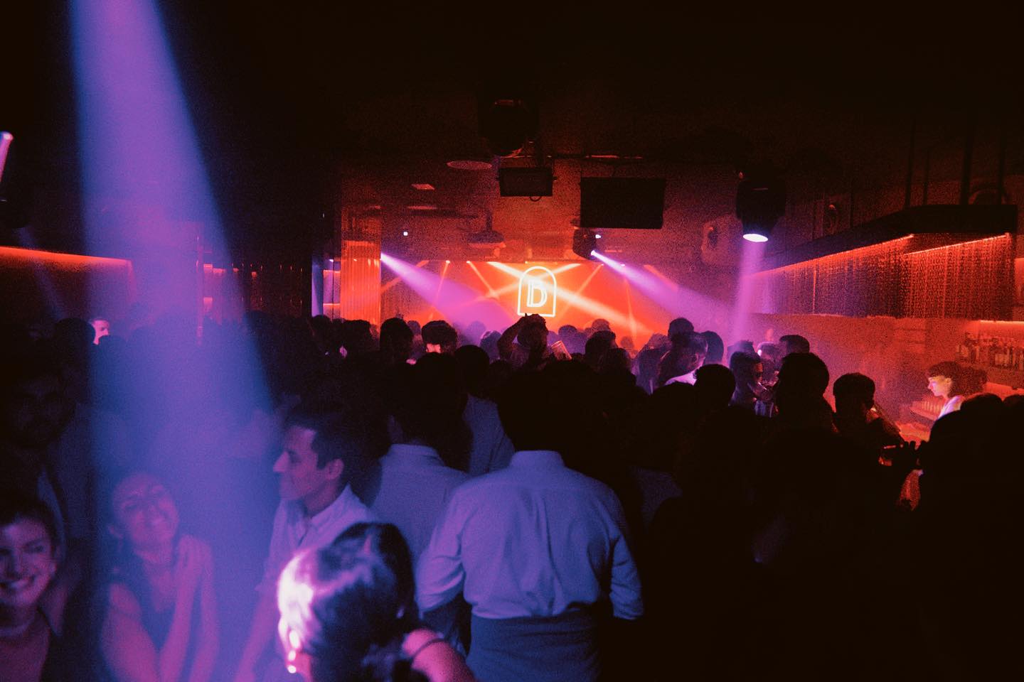 Ambiente vibrante en Sala B, con luces rojas y moradas que iluminan la pista de baile llena de gente disfrutando de la música en un club exclusivo.
