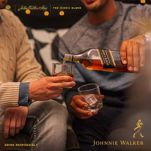 La imagen muestra dos personas cada una con un vaso con whisky Johnnie Walker en la mano y una sirviéndole whisky en el vaso a la otra.