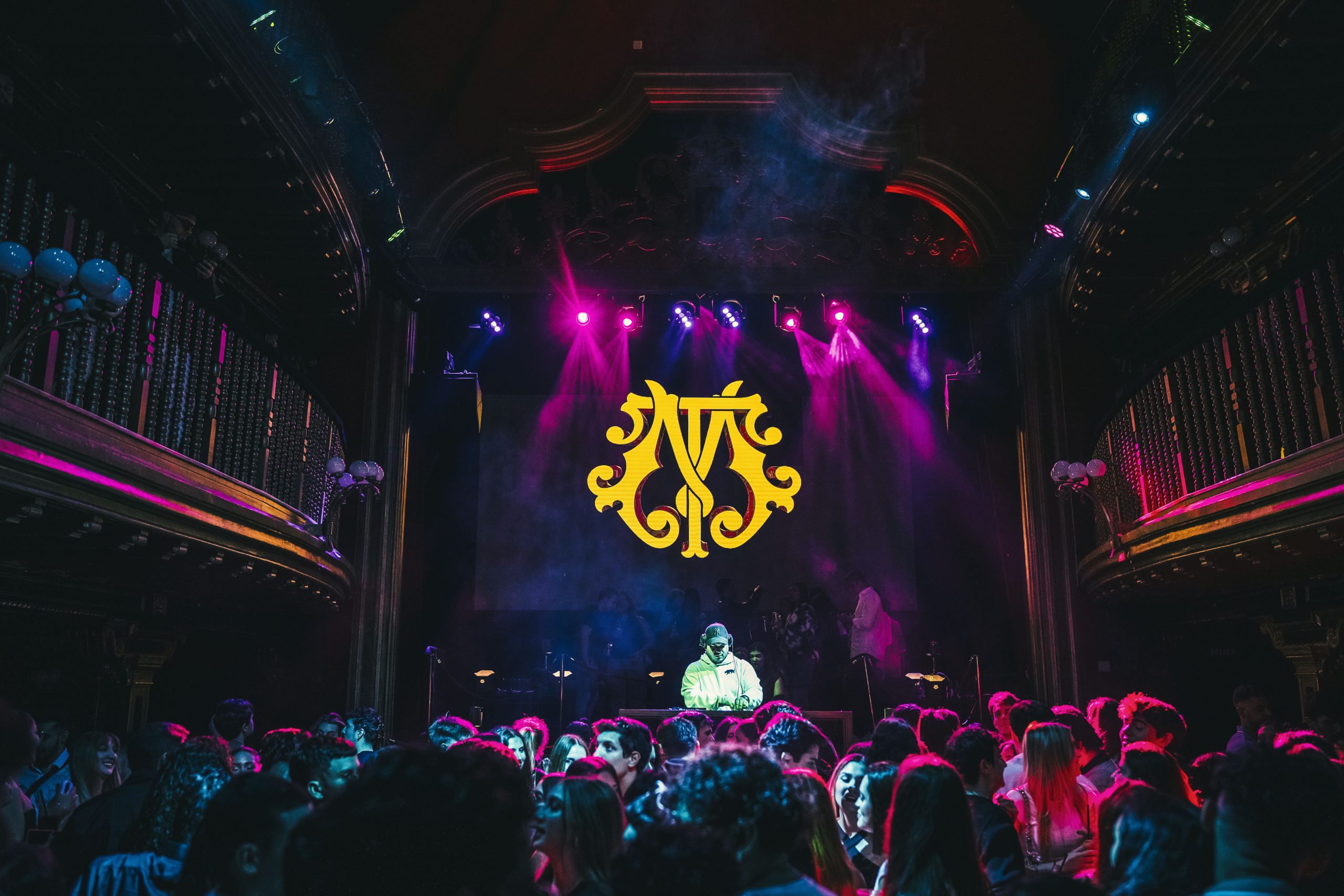 Teatro Magno con un DJ en vivo, luces vibrantes y una multitud disfrutando en un espacio histórico y sofisticado.