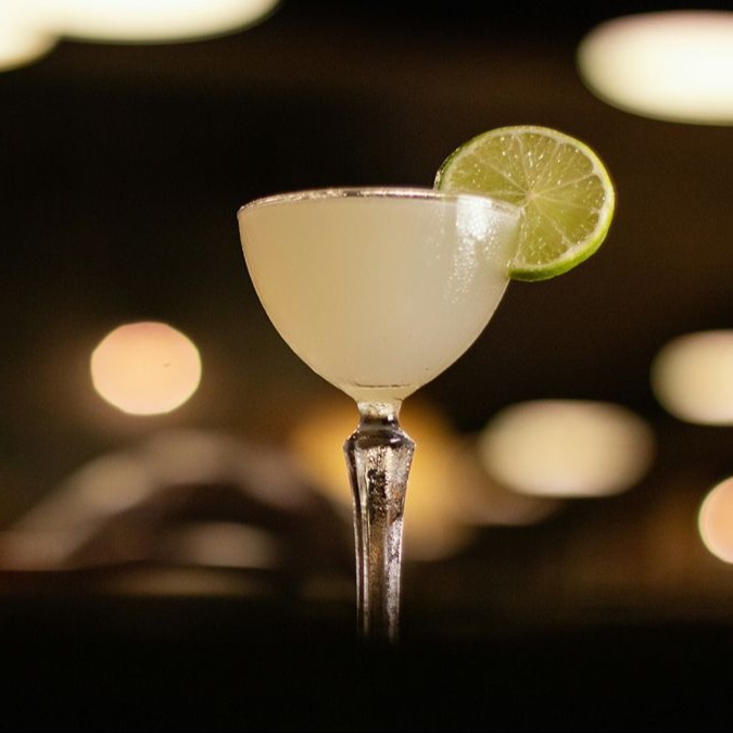 Un cocktail margarita într-un pahar coupe cu o garnitură de roată de lămâie.