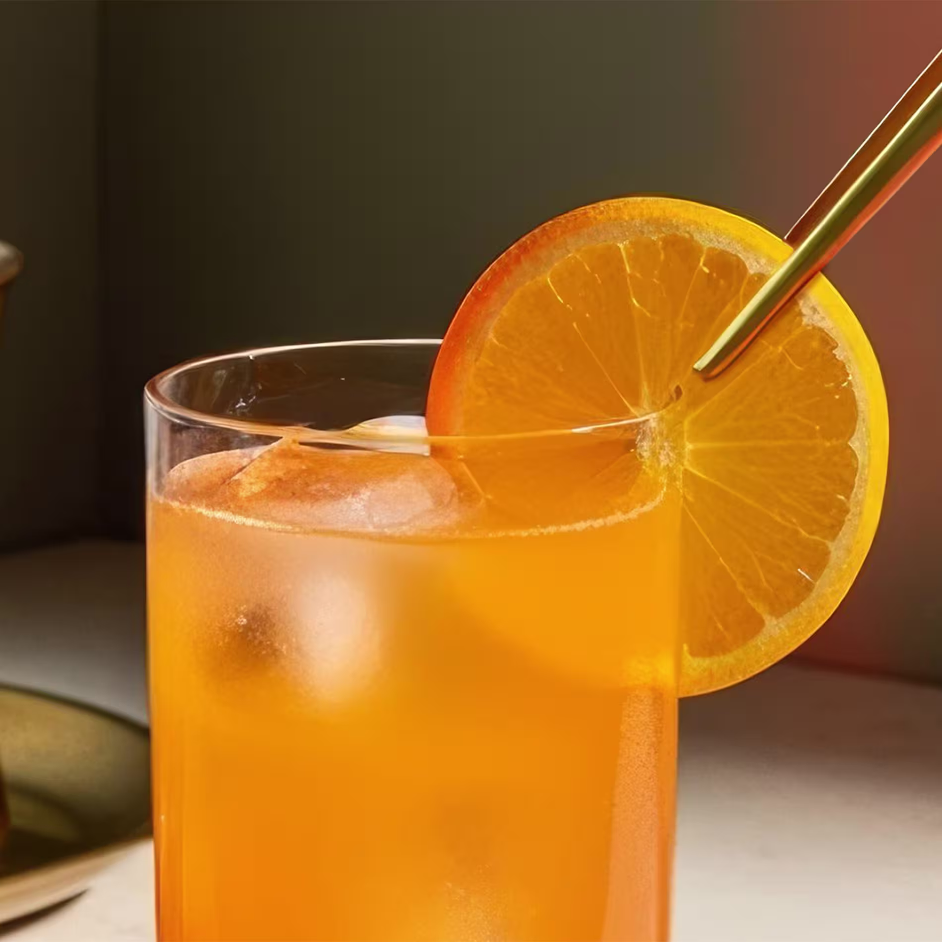 A pair of pincers put an orange slice garnish onto a Harvey Wallbanger cocktail.