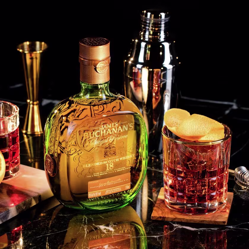 La imagen muestra una botella de whisky Buchanan's 18 años, un vaso con un cóctel preparado con dicho whisky y otros elementos de coctelería.