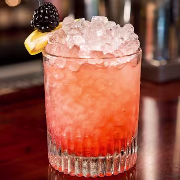 A beautiful Bramble cocktail served in a tumbler with shaved ice and blackberry garnish