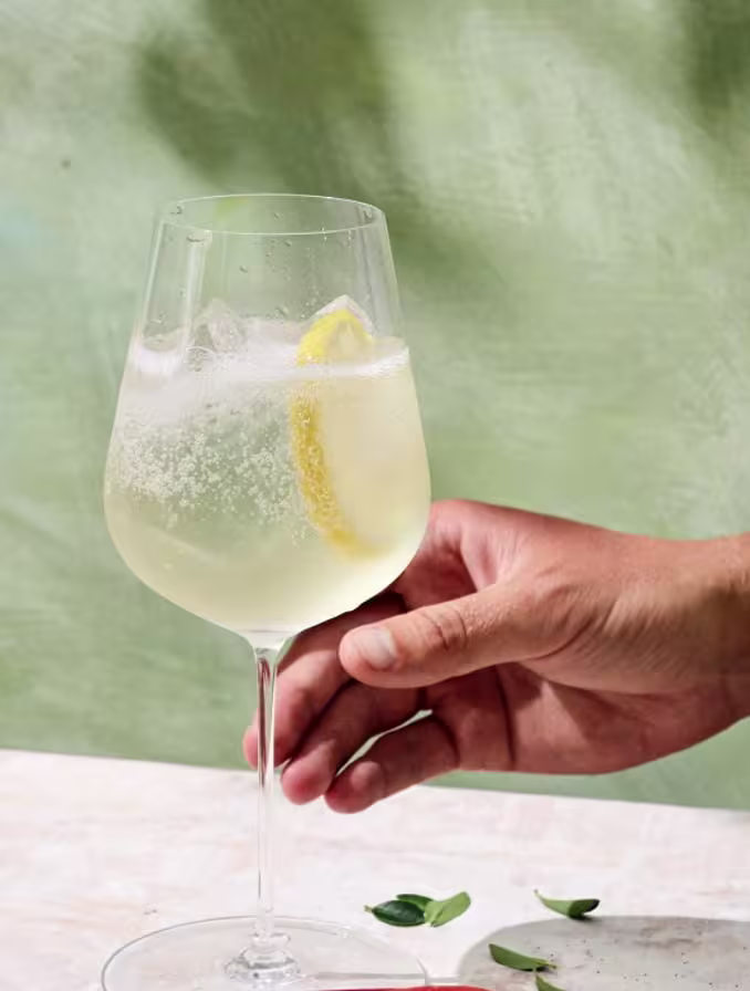 Hand holding a non-alcoholic cocktail in a wine glass with ice and a lemon wedge
