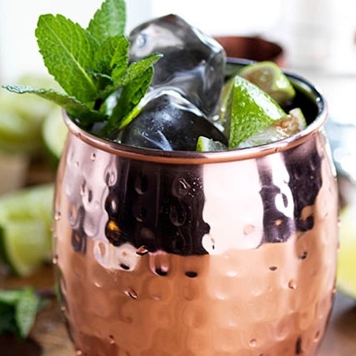 A Moscow Mule in a copper mug with a lime and mint leaf garnish.