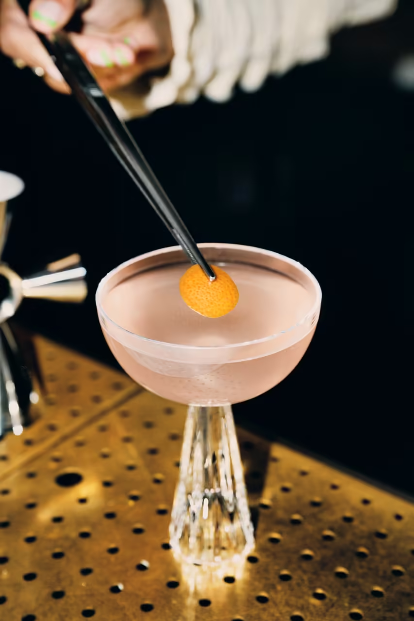 Tweezers placing an orange peel garnish on a Tanqueray No. Ten Gin cocktail