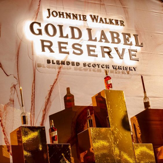 La imagen muestra varias botellas del whisky Johnnie Walker Gold Label Reserve y un cartel luminoso que dice: Johnnie Walker Gold Label Reserve Blended Scotch Whisky.